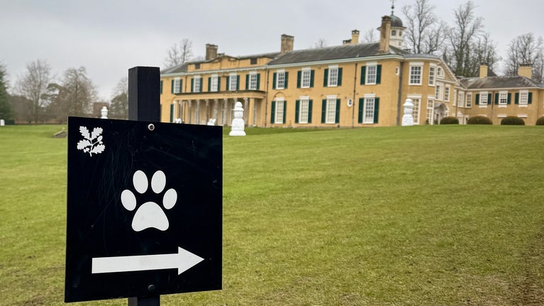A black and white signs indicating where dogs are allowed at Polesden Lacey with the mansion in the background
